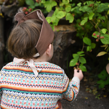 A young child wearing a knitted jumper and a bear dress up fabric crown picks blackberries from the bush.