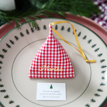 A red gingham fabric fortune cookie with gold personalised name “Martha” sits on a Christmas dinner plate, ready as a handmade festive place setting with a hidden Christmas wish card beneath.