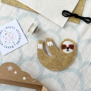 A handmade sloth finger puppet lays beside the craft kit components to make it.