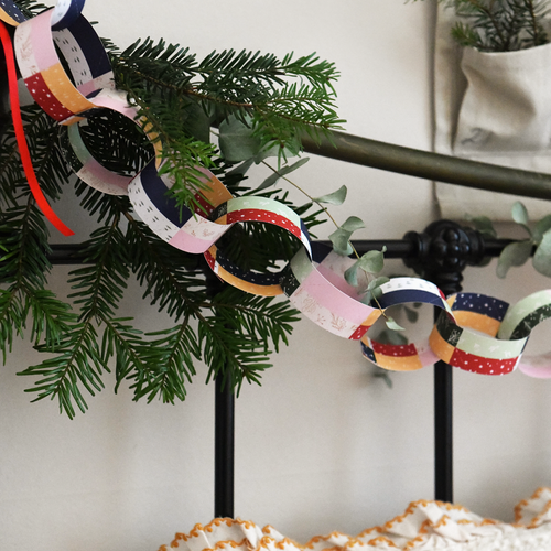 Traditional patchwork design paper chains are strung along the head of a bed along with greenery and red ribbons. An advent calendar hangs above the Christmas paper chains and cosy winter bedding is seen below.