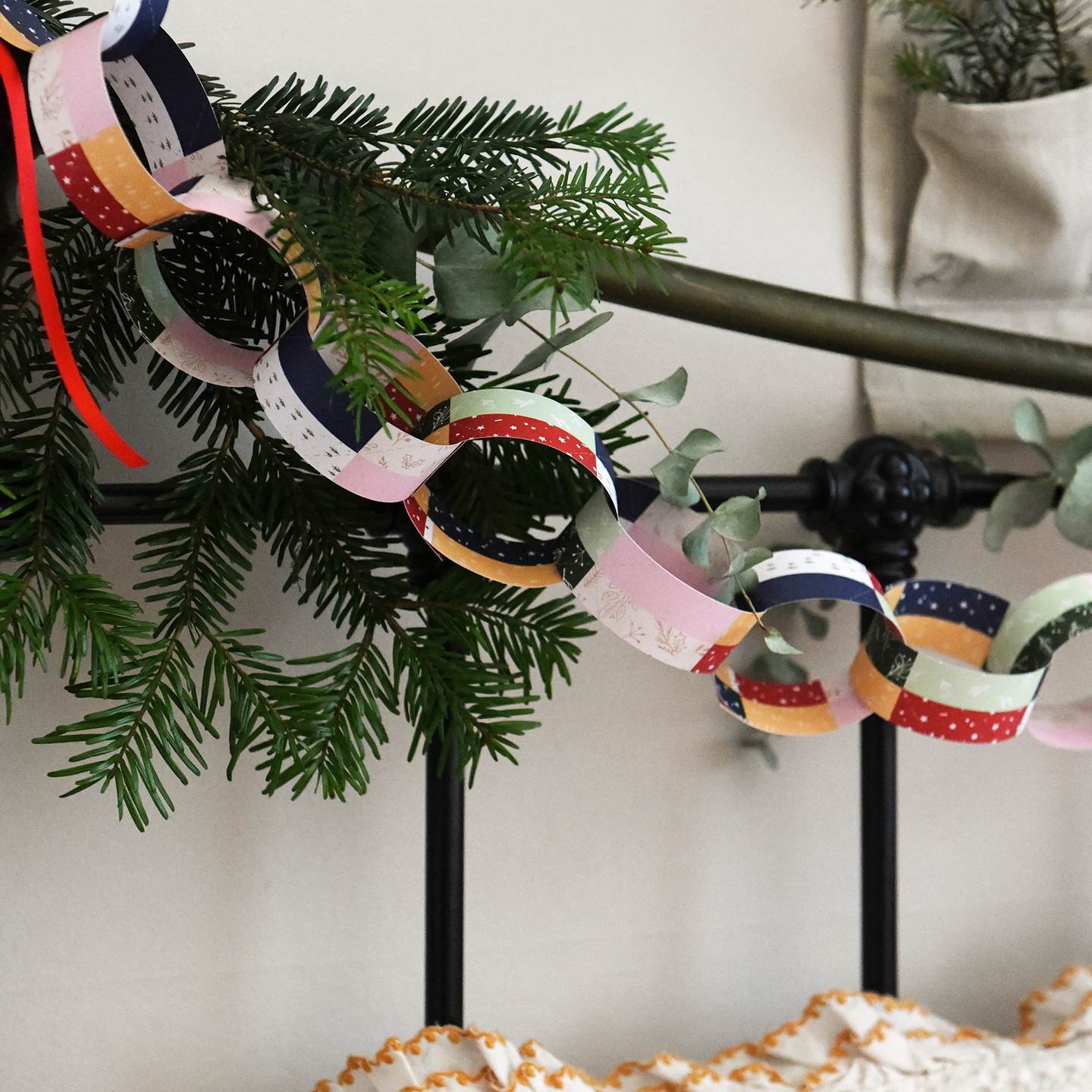 Traditional patchwork design paper chains are strung along the head of a bed along with greenery and red ribbons. An advent calendar hangs above the Christmas paper chains and cosy winter bedding is seen below.