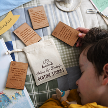 Personalised bedtime story set for dads and children featuring engraved wooden story prompt cards and a drawstring cotton bag reading 'Miles & Daddy’s Bedtime Stories', displayed on a patchwork quilt with a soft toy, picture book, and a young child sleeping beside it.