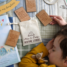 Personalised bedtime story set for dads and children featuring engraved wooden story prompt cards and a drawstring cotton bag reading 'Miles & Daddy’s Bedtime Stories', displayed on a patchwork quilt with a soft toy, picture book, and a young child sleeping beside it.