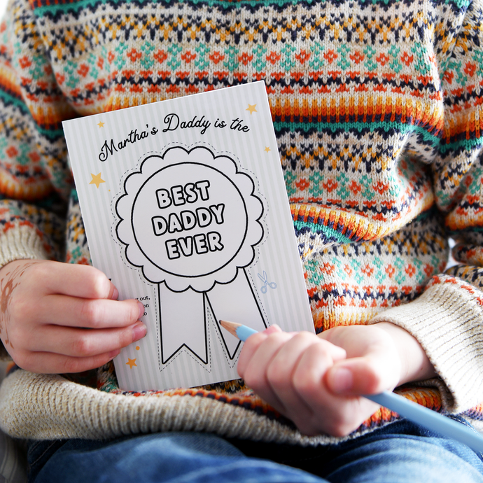 A child wearing a colourful, patterned jumper holds a personalised Father's Day card that reads 
