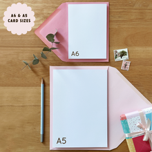 Two greeting cards labeled A6 and A5 on a wooden surface with stationery items.