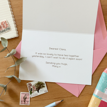 Letter with a pink envelope on a wooden surface with stamps and a pencil.