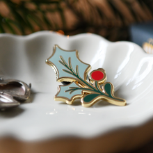 Holly leaf pin with red center on a white dish