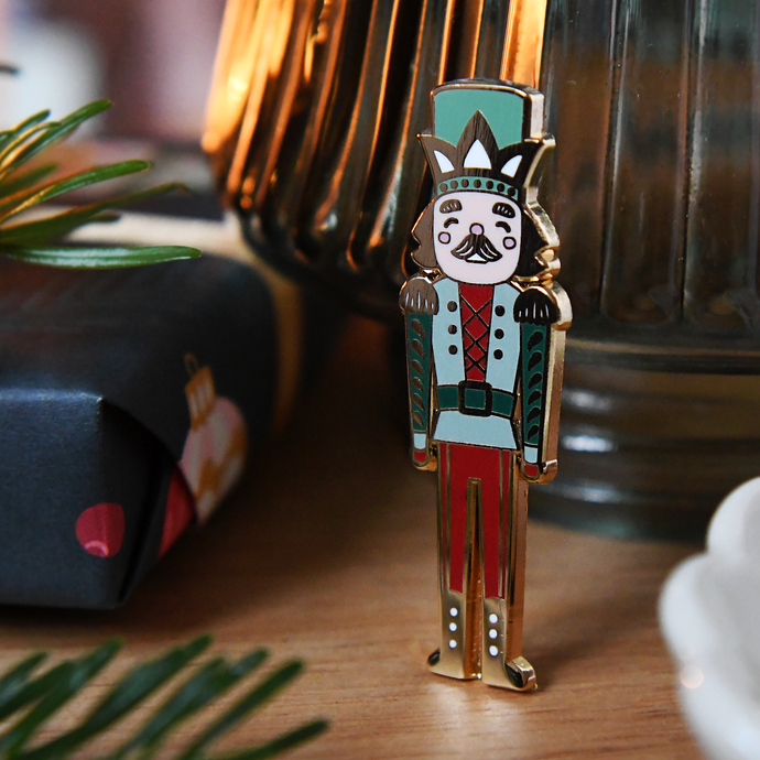 Decorative Christmas nutcracker pin badge on a wooden surface with Christmas decorations in the background.