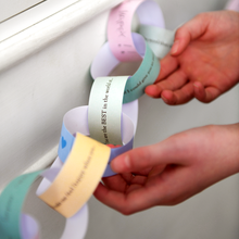 Hands holding a paper chain with motivational phrases against a neutral background