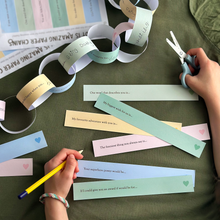 Child completing printable Father's Day paper chain prompts on a green table, creating a colourful Daddy Is Amazing keepsake garland filled with memories and reasons why Dad is loved.