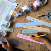 Child completing printable Father's Day paper chain prompts on a wooden table, creating a colourful Daddy Is Amazing keepsake garland filled with memories and reasons why Dad is loved.