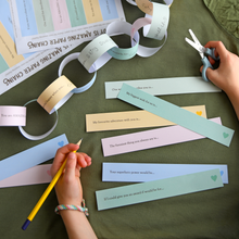 Child completing printable Father's Day paper chain prompts on a green table, creating a colourful Daddy Is Amazing keepsake garland filled with memories and reasons why Dad is loved.