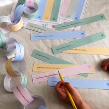 Child completing printable Father's Day paper chain prompts on an ivory fabric surface, creating a colourful Daddy Is Amazing keepsake garland filled with memories and reasons why Dad is loved.