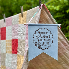 Blue banner with 'Arthur & Daddy's Adventure Club' text hanging on a clothesline with quilts in the background.
