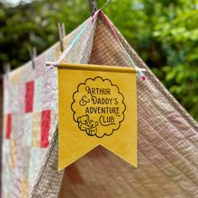 Yellow banner with 'Arthur & Daddy's Adventure Club' text hanging on a clothesline with a tent and quilt in the background.
