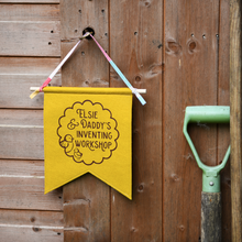 Yellow banner with 'Elsie & Daddy's Inventing Workshop' text hanging on a wooden wall.