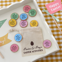A personalised Easter activity bag with the name "Pauline & Posy's Easter Activities" printed on a small cotton drawstring bag. The bag is displayed on a white wooden tray on top of a yellow gingham tablecloth, with colourful wooden activity tokens spread around it, each featuring a fun Easter or spring-themed activity.