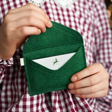 A child wearing a red gingham dress is holding a handmade green felt envelope with a festive notecard tucked inside.