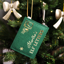 A green felt personalised envelope decoration with golden words reading "Martha's Elf Letters" and a candy cane design stamp in the corner, hangs on a decorated Christmas tree.