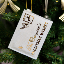 A handmade felt envelope with golden words reading "The Clempson's Christmas Wishes" and a reindeer design stamp in the corner, hangs on a decorated Christmas tree.