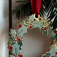 An heirloom Christmas wreath decoration with holly leaves and red berries hangs from a red ribbon on a white door handle.