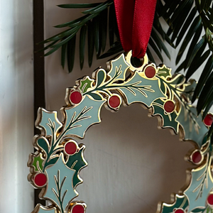 An heirloom Christmas wreath decoration with holly leaves and red berries hangs from a red ribbon on a white door handle.