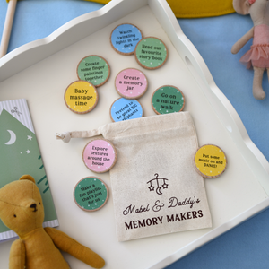 A flat lay of “Mabel & Daddy’s Memory Makers” eco-friendly activity tokens displayed on a white tray, featuring a drawstring cotton bag and colourful wooden discs with bonding prompts like “Go on a nature walk” and “Put some music on and DANCE!”. Ideal for new dads celebrating their first Father’s Day with their baby.