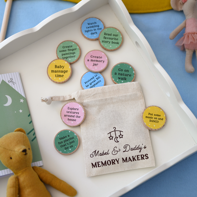 A flat lay of “Mabel & Daddy’s Memory Makers” eco-friendly activity tokens displayed on a white tray, featuring a drawstring cotton bag and colourful wooden discs with bonding prompts like “Go on a nature walk” and “Put some music on and DANCE!”. Ideal for new dads celebrating their first Father’s Day with their baby.