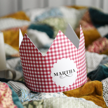 A red gingham Christmas crown, with a scalloped circle on the front and the name Martha, rests on a cosy patchwork quilt.