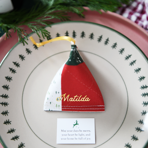 A traditional patchwork design fabric fortune cookie with gold personalised name “Matilda” sits on a Christmas dinner plate, ready as a handmade festive place setting with a hidden Christmas wish card beneath.