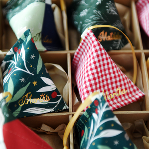 A Christmas decorations box full of handmade fabric fortune cookie decorations, each from a different festive fabric and with a personalised name in gold lettering, with a gold ribbon. 