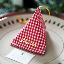 A red gingham fabric fortune cookie with gold personalised name “Martha” sits on a Christmas dinner plate, ready as a handmade festive place setting with a hidden Christmas wish card beneath.
