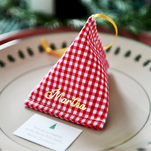 A red gingham fabric fortune cookie with gold personalised name “Martha” sits on a Christmas dinner plate, ready as a handmade festive place setting with a hidden Christmas wish card beneath.