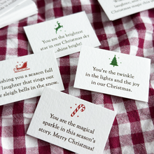 Several tiny Christmas wish cards, each with a festive illustration and a written Christmas wish on, lay on a red gingham fabric surface.